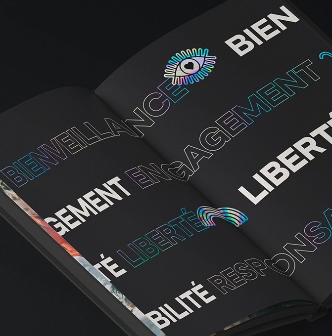 Un livre ouvert aux pages noires affiche de grands mots en gras en français tels que BIENVEILLANCE, ENGAGEMENT et LIBERTÉ dans des polices de caractères colorées, soulignées et remplies, ainsi que l'image d'un œil.