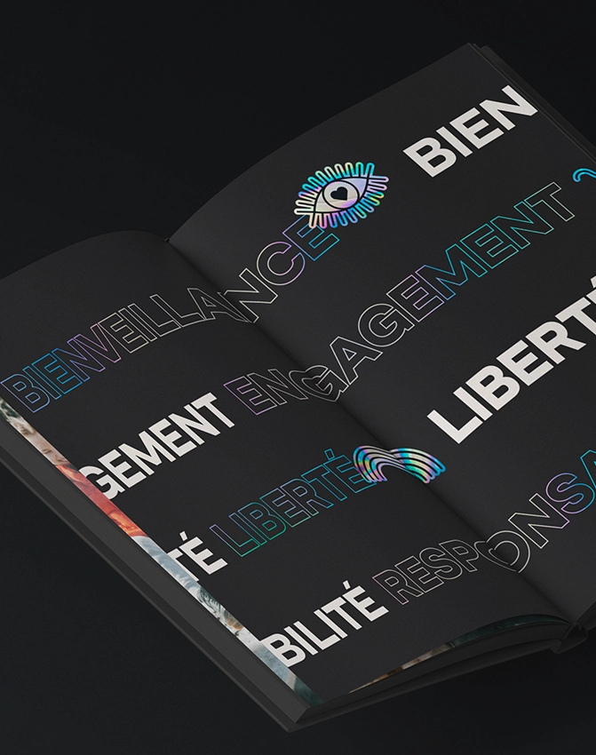 Un livre ouvert aux pages noires affiche de grands mots en gras en français tels que BIENVEILLANCE, ENGAGEMENT et LIBERTÉ dans des polices de caractères colorées, soulignées et remplies, ainsi que l'image d'un œil.